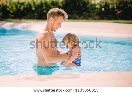 little cute blonde baby girl playing with father in pool