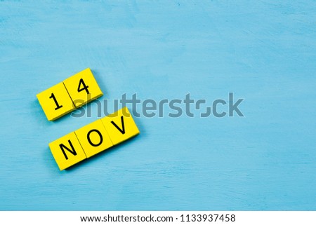 NOV 14, yellow cube calendar on blue wooden surface with copy space