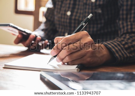 Asian young business man of student holding a pen writing letter on paperand using mobile phone at home
