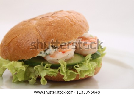delicious fast-food soft burger with tasty shrimps dipped in white fresh sauce,green fresh cucumbers,crispy green lettuce leaves and mayonnaise with a little ketchup on a white round plate