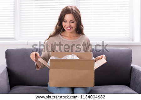 Smiling Young Woman Sitting On Sofa Unpacking Received Parcel