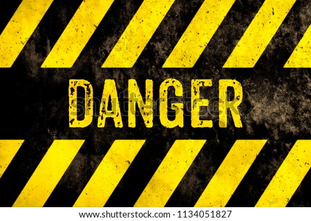Danger warning sign text with yellow and black stripes painted over concrete wall surface facade texture background. Concept image for caution, dangerous area and hazard.