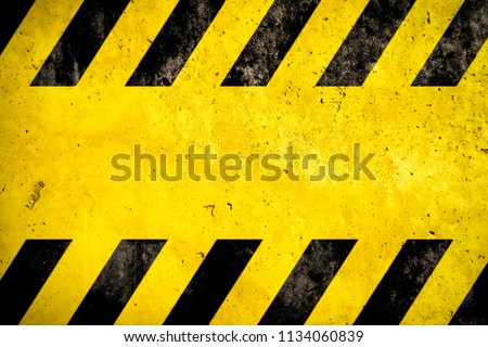 Warning danger background with yellow and black stripes painted over yellow concrete wall facade texture and empty space for text message in the middle. Concept image for caution, danger and hazard. Royalty-Free Stock Photo #1134060839