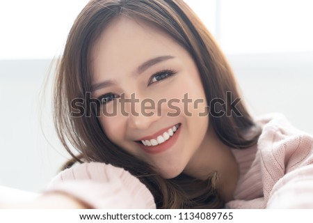 Closeup portrait of inspired caucasian Asian lady wearing knitted sweater pink cold smiling and taking selfie at her home.Concept woman lifestyle and winter. Fashion, Autumn, winter season.