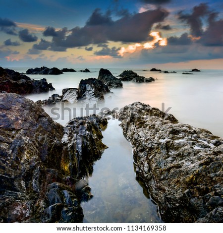 A long exposure picture Beautiful Scenery cloudy Sunset With Stone and wave As Foreground
