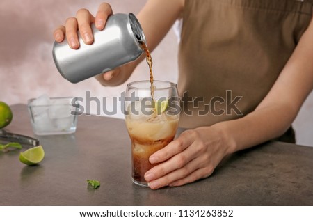 Woman pouring cola from tin can into glass at table