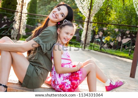 Beautiful mother and daughter sitting outdoors, laughting and having fun. Concept of happy family