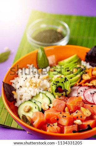 Hawaiian salad Poke with salmon fish, avocado, Korean carrots, cucumbers, radish and rice, with black sesame. in an orange plate. On the purple trend background of 2018. copy space, top view