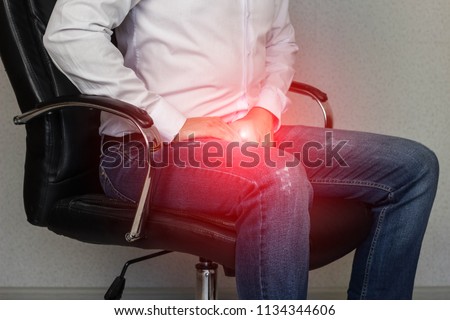 A man sits in an office chair and holds on to the groin, crotch, prostatitis Royalty-Free Stock Photo #1134344606