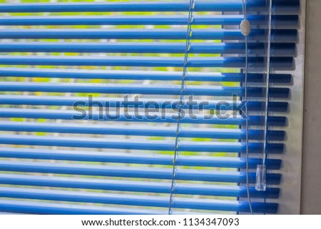 Closeup blue jalousie,curtain, Louvers , shade or shutter background open slightly see the green color of trees blurred.