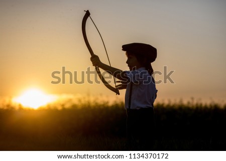 Portrait of child playing with bow and arrows, archery shoots a bow at the target on sunset Royalty-Free Stock Photo #1134370172