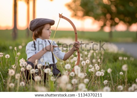 Portrait of child playing with bow and arrows, archery shoots a bow at the target on sunset Royalty-Free Stock Photo #1134370211