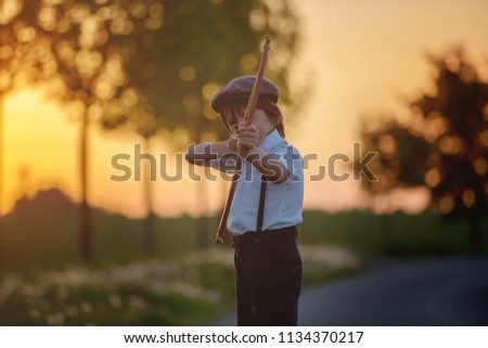 Portrait of child playing with bow and arrows, archery shoots a bow at the target on sunset Royalty-Free Stock Photo #1134370217