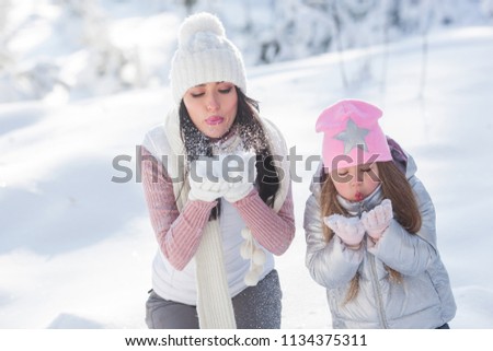 Young mother and her daughter having fun in the snow