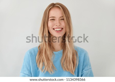 Smiling satisfied female with broad shining smile, feels happiness after successful graduation, wears casual outfit, stands against white background. Glad woman rejoices unforgettable journey
