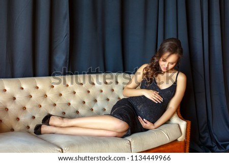 pregnant girl sitting on the couch in a beautiful dress