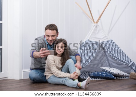 Father and daughter taking selfie playing at home with constructed wigwam