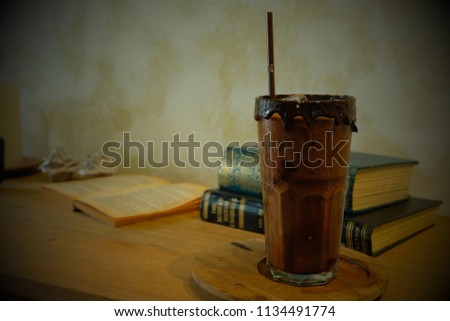 A glass of iced mocha or chocolate near books on the table in retro filter 