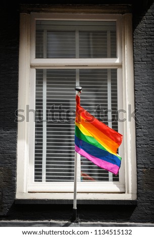 Gay flag on a pole installed on a building exterior in Amsterdam.  Royalty-Free Stock Photo #1134515132