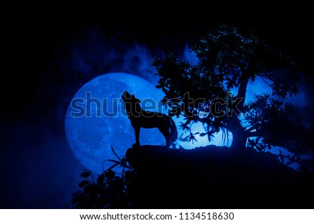 Silhouette of howling wolf against dark toned foggy background and full moon or Wolf in silhouette howling to the full moon. Halloween horror concept. Selective focus