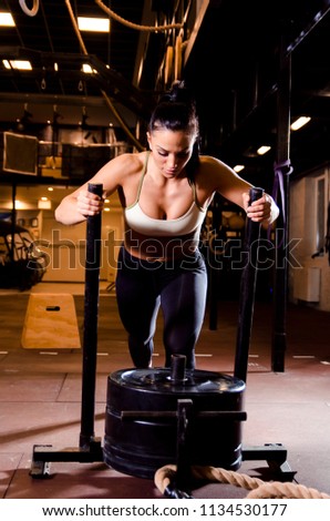 Strong young female pushing sleds in gym 