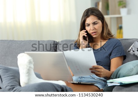 Angry disabled self employed claiming on phone sitting on a couch in the living room at home Royalty-Free Stock Photo #1134530240