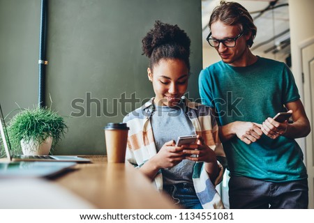 Positive multiracial friends share multimedia files via smartphone bluetooth connection on free time, cheerful male and female students talking and watching video on mobile phone online together Royalty-Free Stock Photo #1134551081