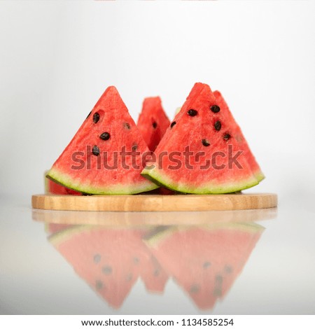 Berry watermelon in water splashes on a wooden tray. Reflection on table.