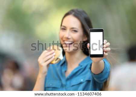Woman holding a burger showing a blank phone screen mock up on the street