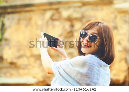 Portrait of a cute asian teenager young woman stand against blurred vintage ancient temple place. wearing sunglasses. take a photo with smartphone. light effect added. travel hipster concept
