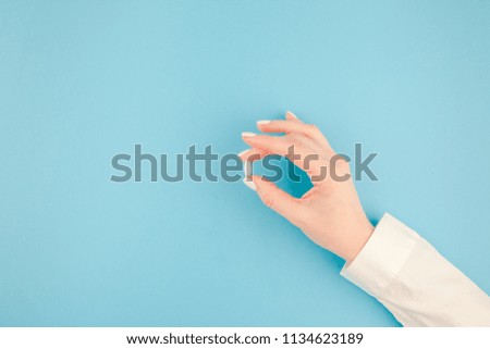 Woman hand holding a white pill on pastel blue paper background with copy space in minimal style, template for text. Concept of medical treatment, pharmacy, healthcare.