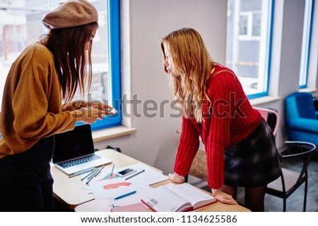 Serious african hipster girl making images of fashion sketches on smartphone camera spending time with trendy female friend on course work and design education, concept of technology and communication