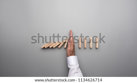 Top view of male hand in white shirt stopping falling dominos on gray desk. Royalty-Free Stock Photo #1134626714
