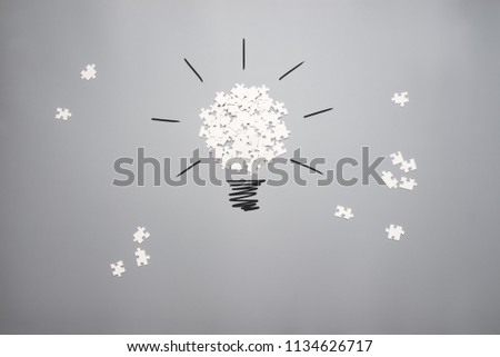 Conceptual image of vision and idea with a pile of white scattered puzzle pieces forming a light bulb on a grey background.