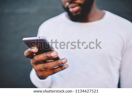 Cropped image of african american man holding modern smartphone dialing number, dark skinned male in white shirt using mobile phone for chatting in social networks via 4G internet connection outdoors Royalty-Free Stock Photo #1134627521
