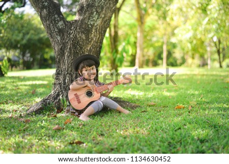 Asian little kid girl playing guitar or ukulele in the garden. Music,musician and guitarist concept.