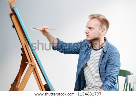 young male artist with a brush and canvas paints a picture in the studio.