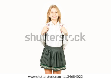 Beautiful blonde teenage girl with charming smile in schoolgirl uniform wearing pleated skirt, white shirt, hands on backpack straps. Back to school sale concept. Background, copy space, close up.