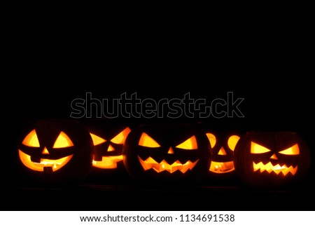 Many Halloween Pumpkin glowing faces in a row isolated on black background