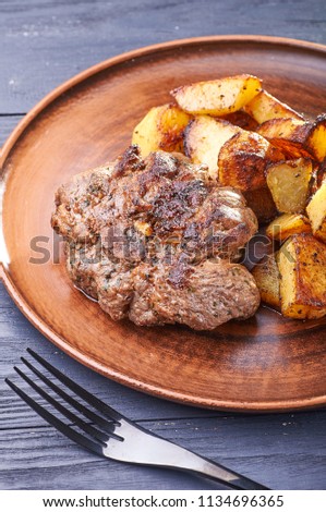 Appetizing piece of fried meat on a large clay plate. Fried potatoes with crispy crust on garnish. Tables are served for lunch and dinner at home, in a restaurant, in the cafe.