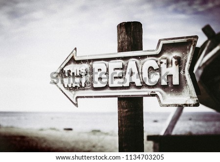 Vintage artistic color arrow shaped sign showing way to the beach, on the pole on the beach, sea background.