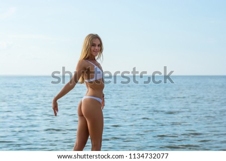 Beautiful happy young woman in a white swimsuit stands at sea background