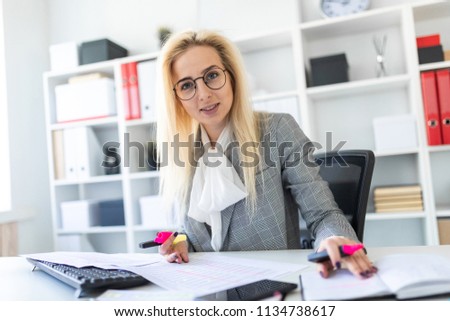 A young girl in glasses works in the office with a marker, a notebook and documents.