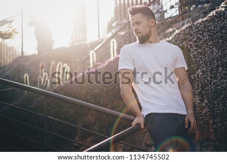 Awesome hipster guy in a light t-shirt standing in the beams of a sunset. Horizontel mock-up.