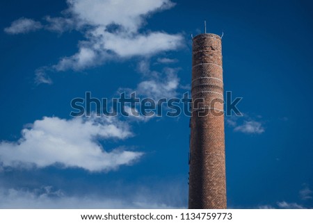 Tall brick round industrial chimney on a sunny day with blue sky as a background with some puffy white clouds