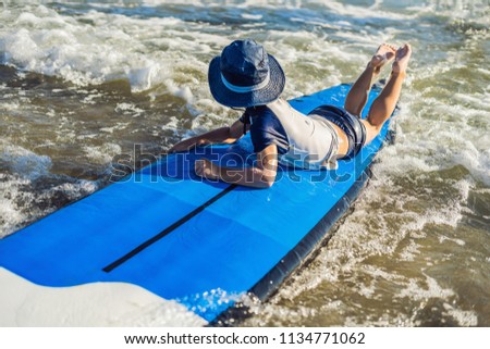 Happy baby boy - young surfer ride on surfboard with fun on sea waves. Active family lifestyle, kids outdoor water sport lessons and swimming activity in surf camp. Summer vacation with child.