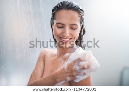 Portrait of happy girl taking shower with gel. She washing with puff Royalty-Free Stock Photo #1134772001