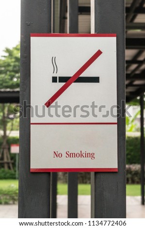 No smoking sign stuck to the pole in the park, black cigarette with red line over on it on white background
