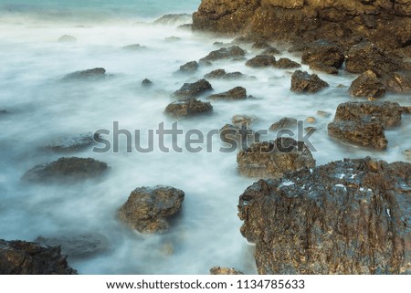 Long exposure seascape with foamy waves splashing against a rocky shore of thailand in the morning time