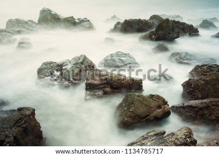 Long exposure seascape with foamy waves splashing against a rocky shore of thailand in the morning time
